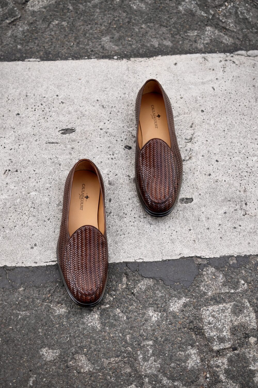 A pair of brown woven slip-on shoes placed on a crosswalk.