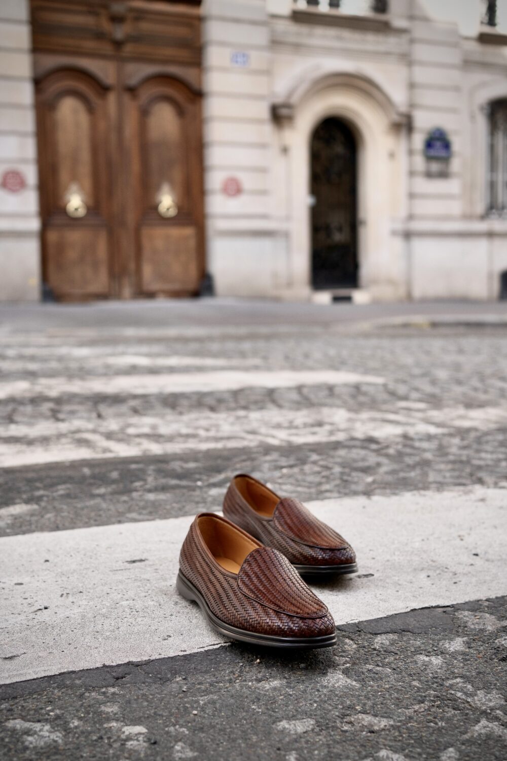 A pair of brown woven loafers placed on a white crosswalk.