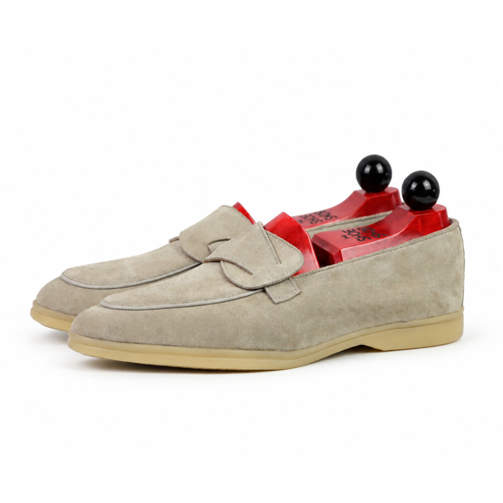 A pair of light gray suede loafers with a decorative strap and red shoe trees inside.