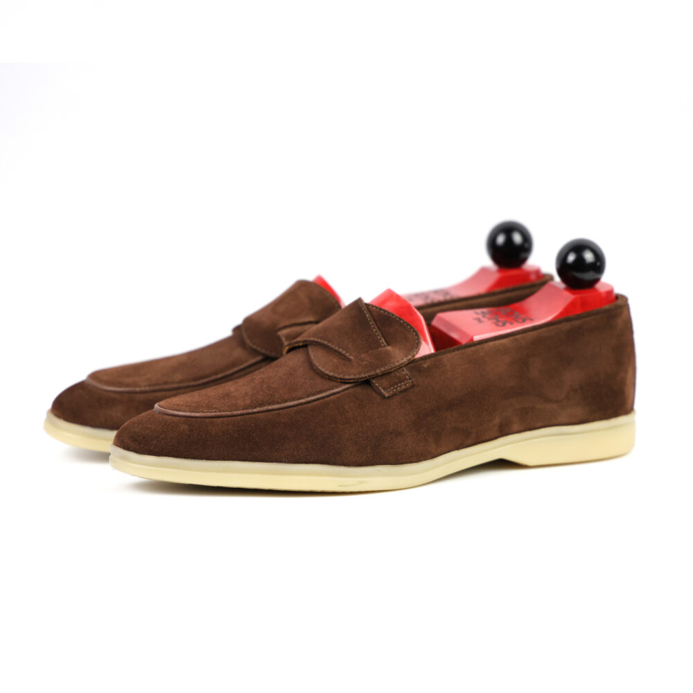 Brown suede loafers with a decorative flap and contrasting red insoles.