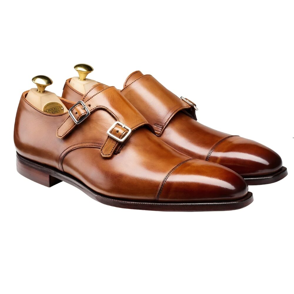 A pair of polished brown leather double monk strap shoes with silver buckles.