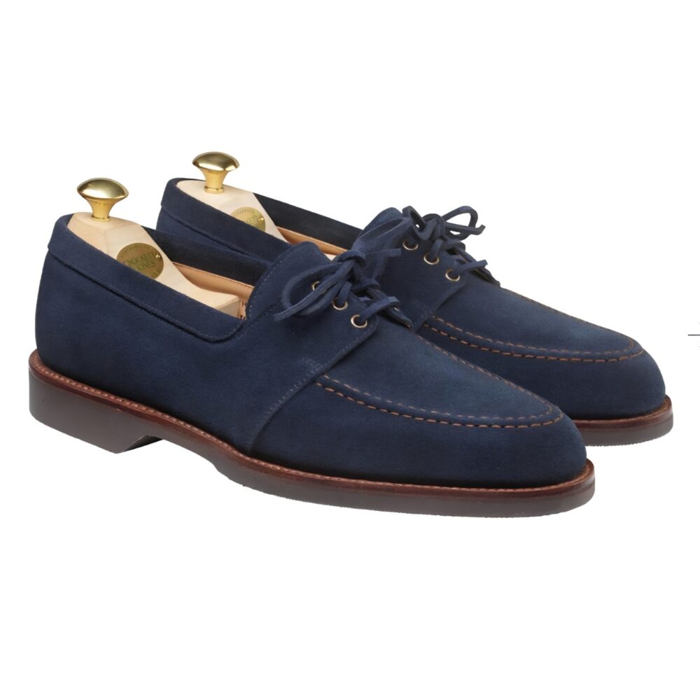 A pair of navy blue suede shoes with a brown sole and gold shoe trees inserted.