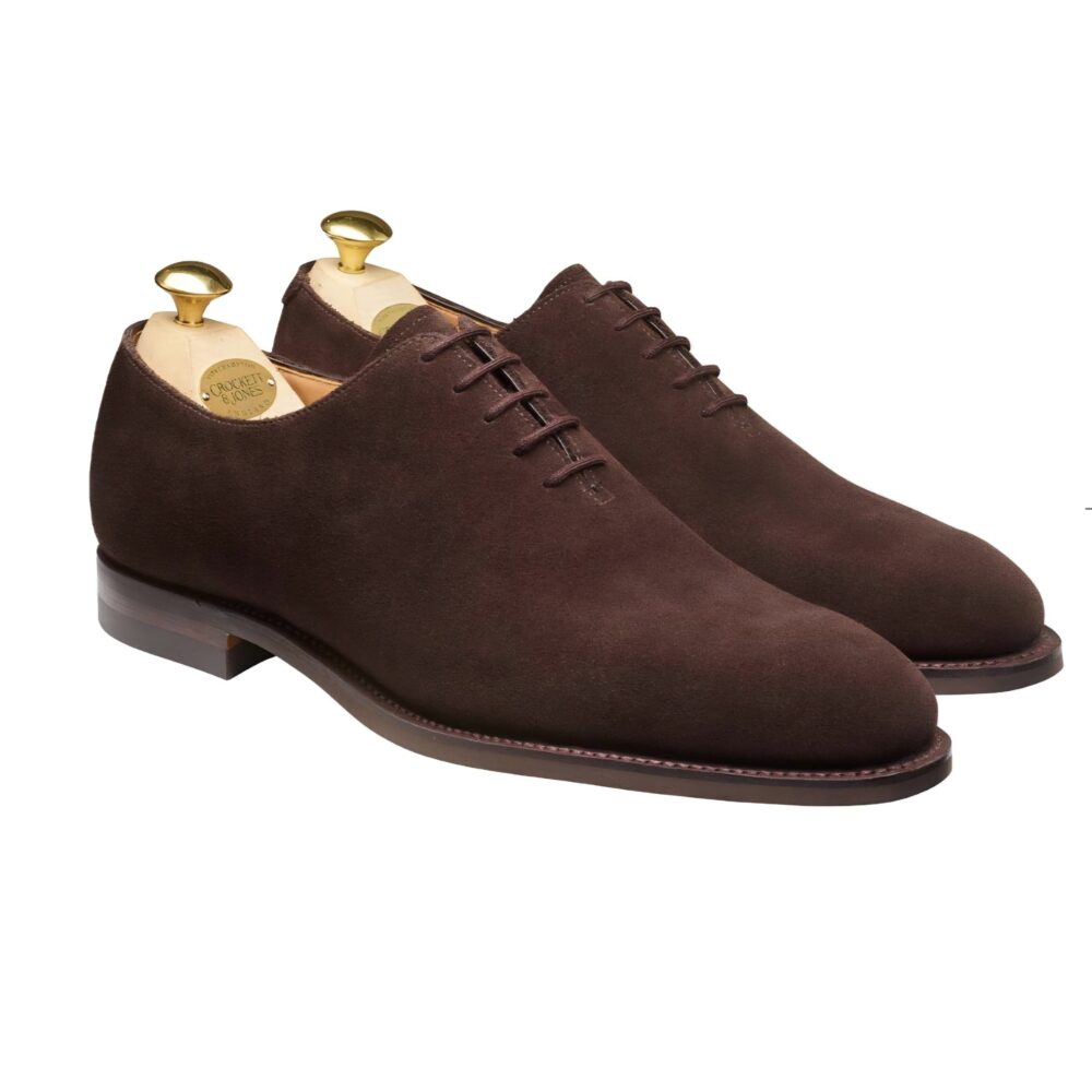 A pair of brown suede shoes with leather soles and gold shoehorns inside.