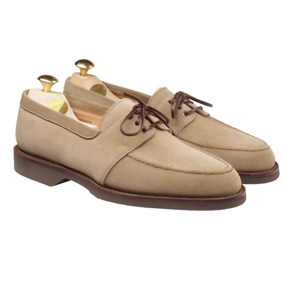 A pair of beige suede shoes with brown laces and wooden shoe trees inside.