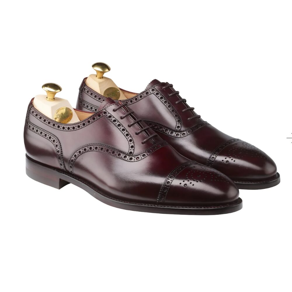 A pair of burgundy leather dress shoes with decorative brogue detailing and shoe trees inserted.