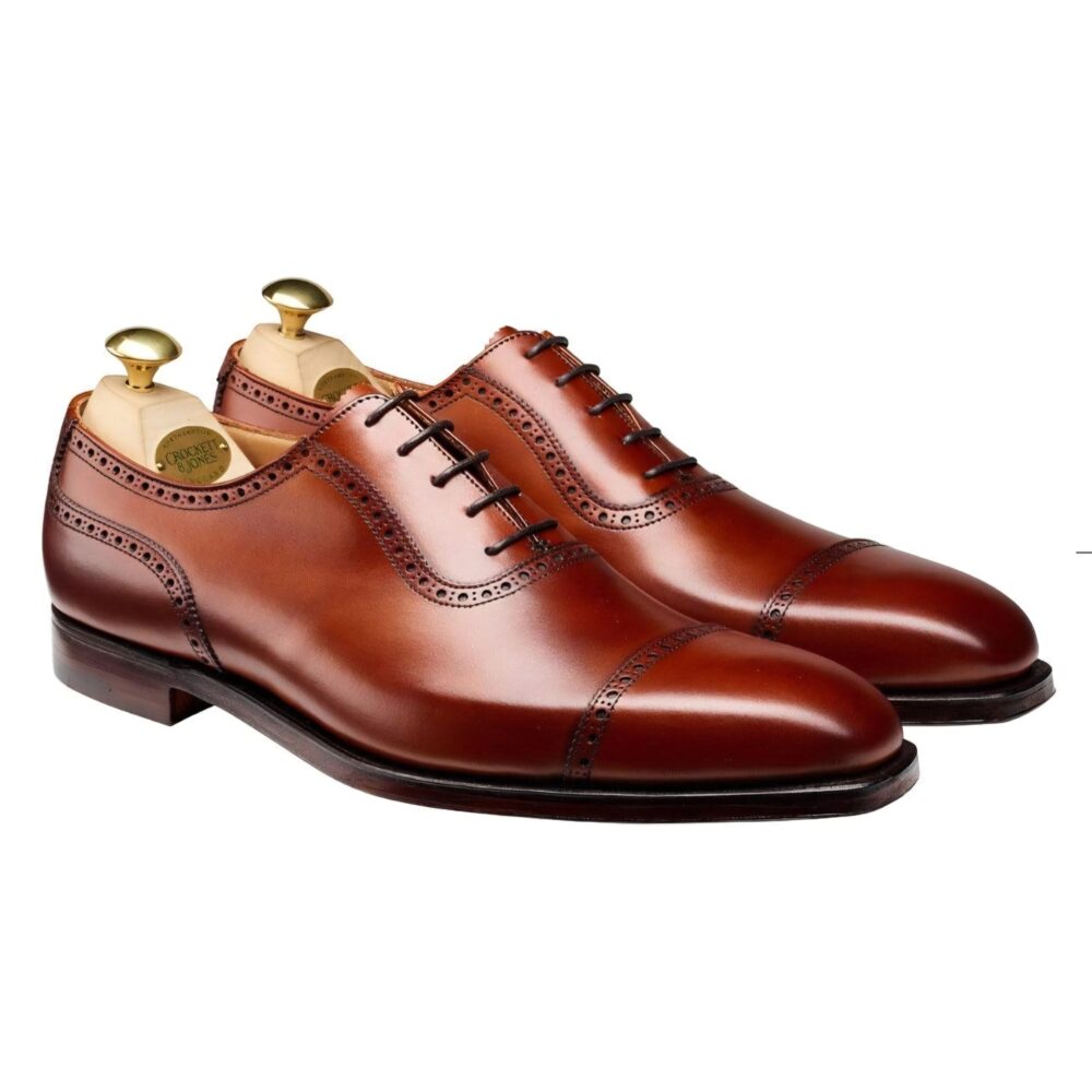 A pair of polished brown leather dress shoes with decorative perforations and shoe trees inside.