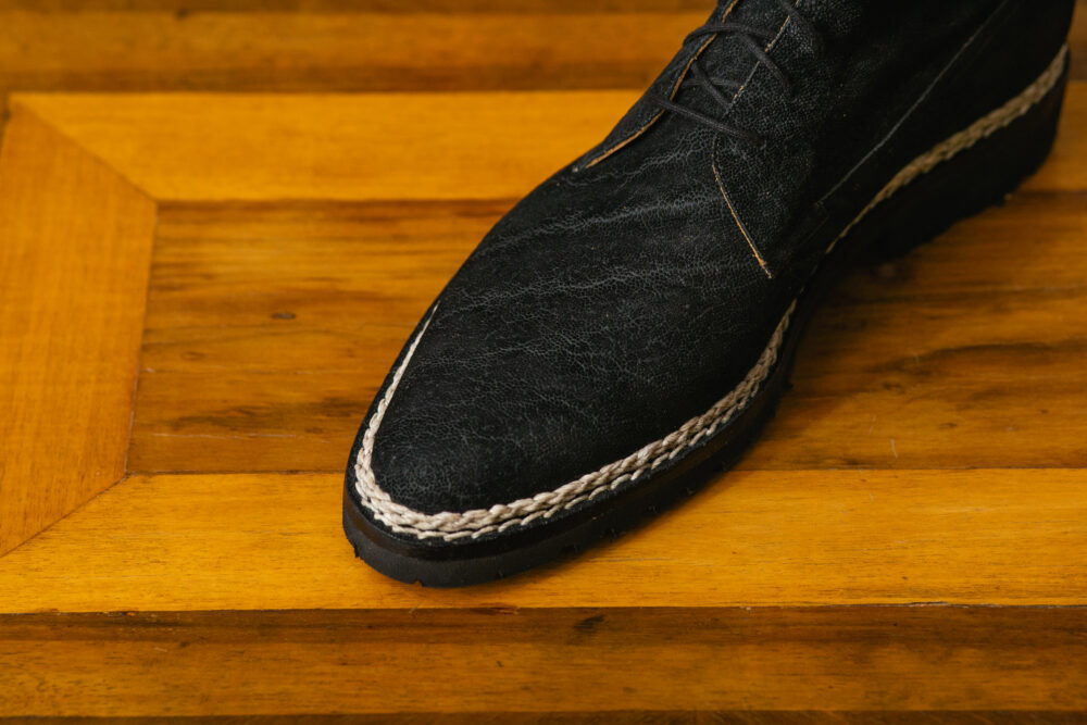 A close-up of a black leather shoe with a braided white trim along the sole.