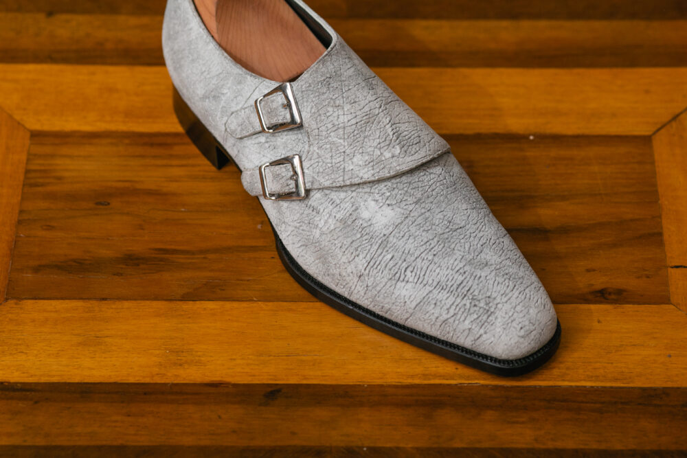 A close-up of a gray leather dress shoe with two silver buckles.