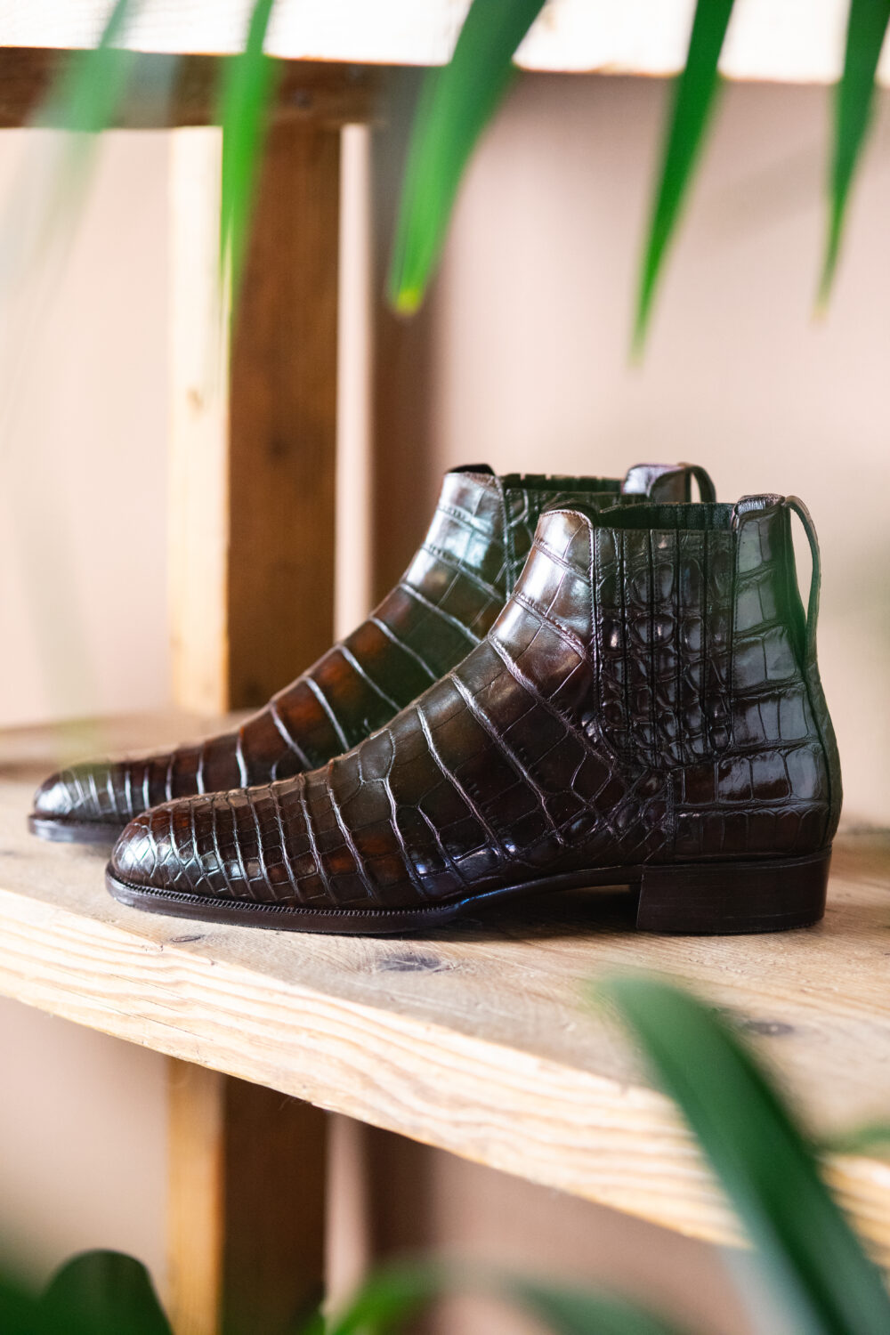 A pair of dark brown, crocodile-patterned leather ankle boots on a wooden shelf.