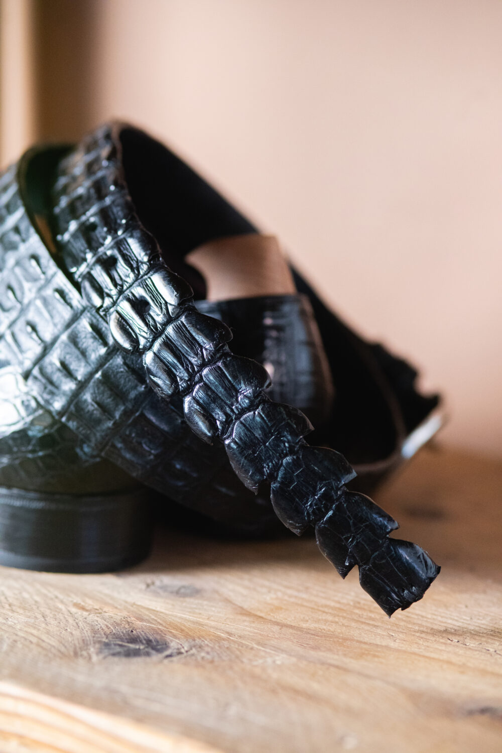 A close-up of a black crocodile-embossed leather shoe with a decorative strap.