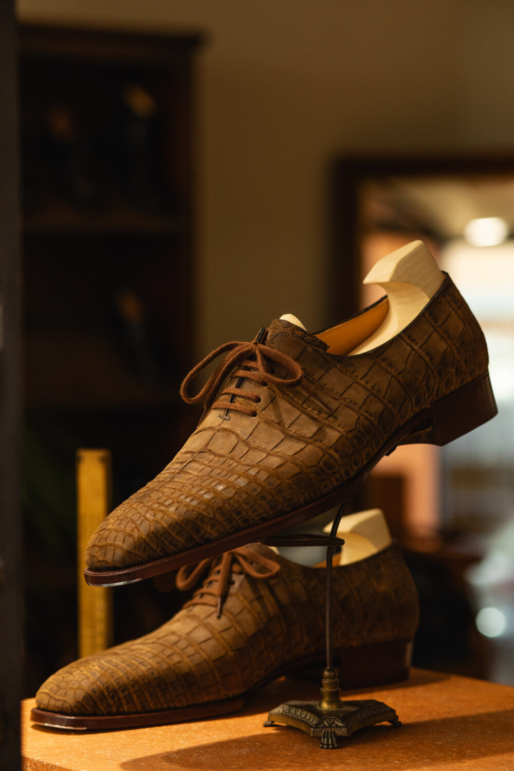 A pair of brown crocodile-patterned dress shoes with laces displayed on a stand.