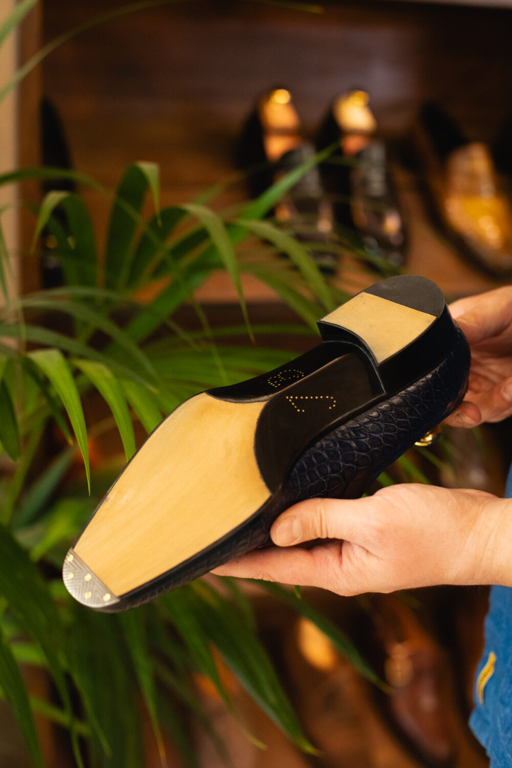 A person holds a navy blue shoe sole with a wooden base and a black textured side.