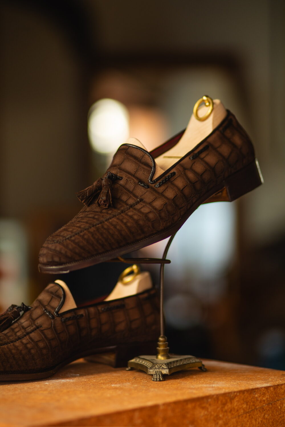 A pair of brown crocodile-patterned loafers displayed on a stand.