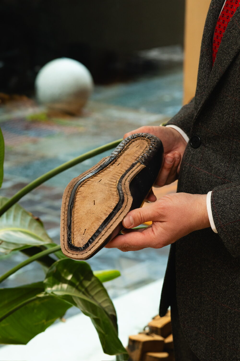 A person holds a black leather shoe sole with visible stitching and a beige interior.