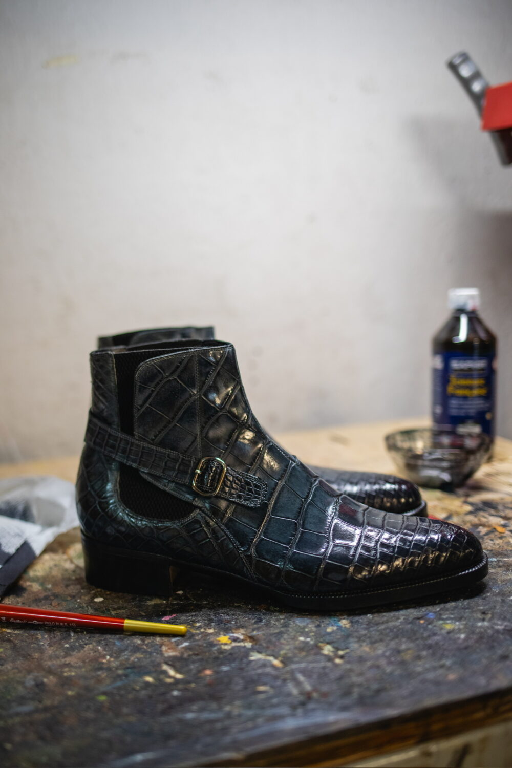 A pair of black crocodile leather ankle boots with a buckle detail.