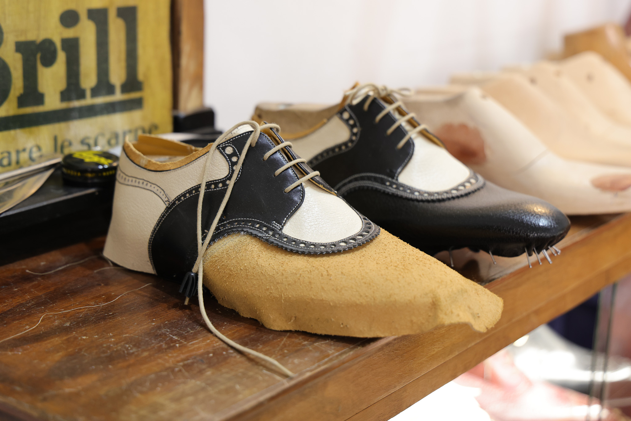 A pair of handcrafted shoes featuring a black leather upper and a beige leather body with a suede toe.