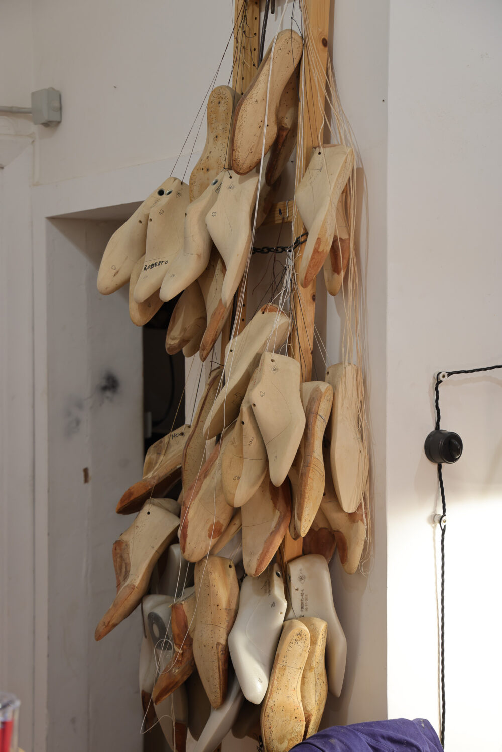 A collection of wooden and plastic shoe lasts, some marked with numbers and names, hanging on a wooden rack.