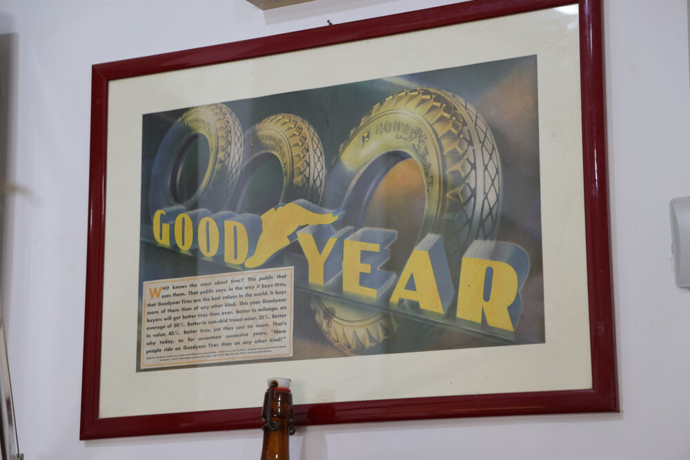 A framed advertisement featuring the text "GOOD YEAR" in large yellow letters, with three Goodyear tires displayed above it.