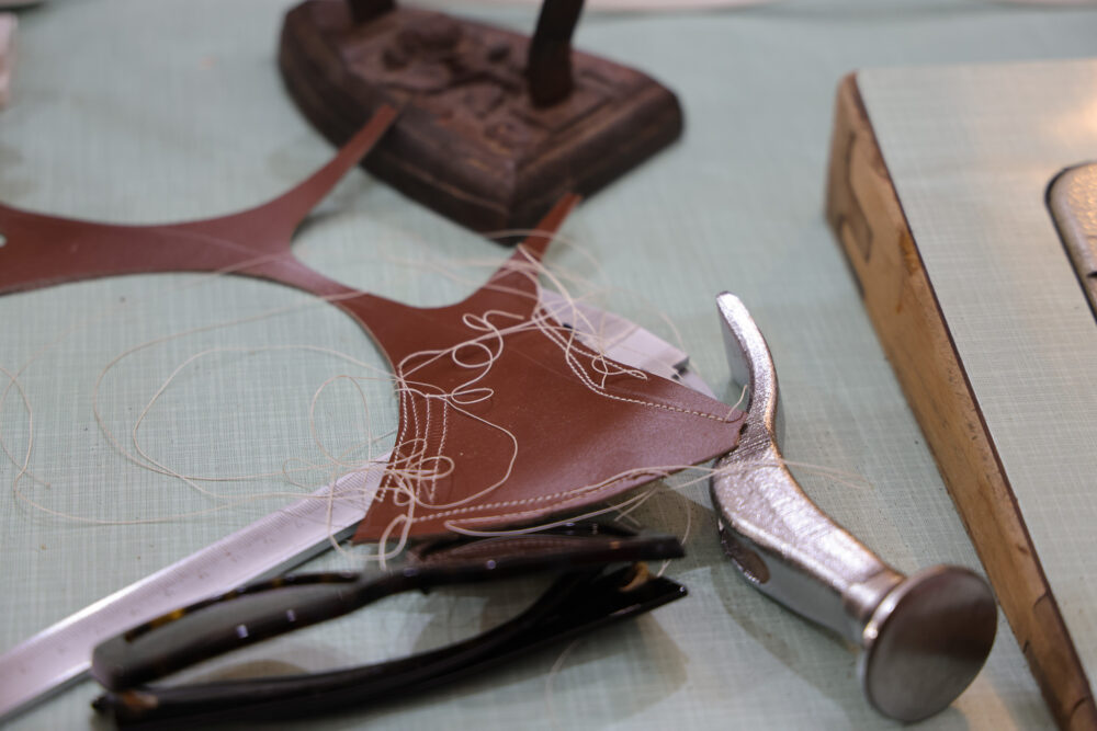 A brown leather piece with white thread and a silver hammer on a light green surface.