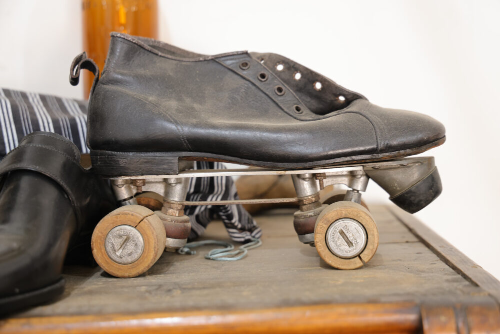 A black leather shoe mounted on a metal roller skate frame with wooden wheels.