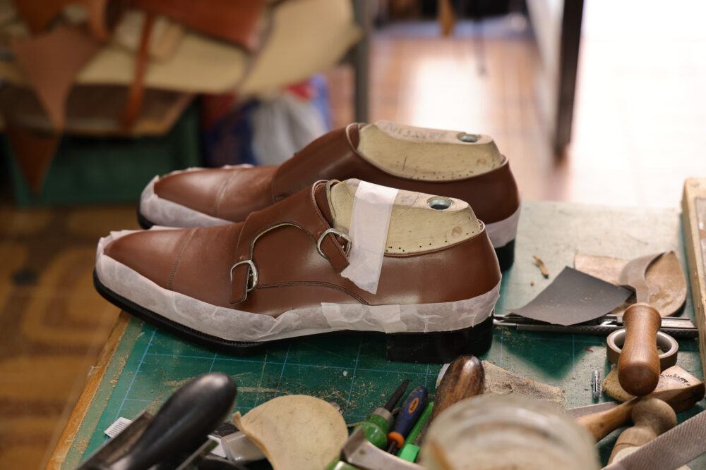 A pair of brown leather shoes with white protective paper around the soles is displayed on a workbench.