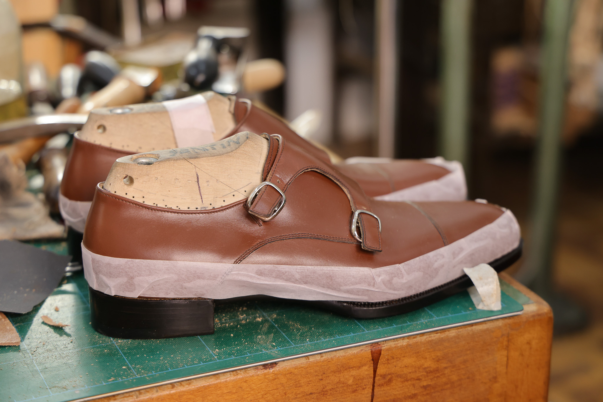 A pair of brown leather shoes with silver buckles, resting on a green cutting mat.