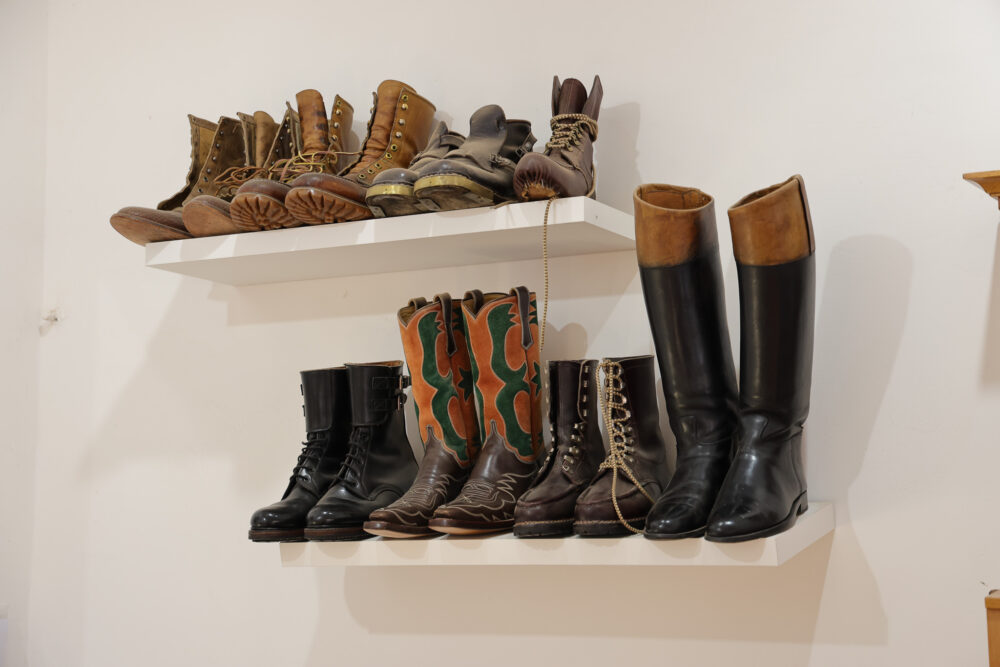 A variety of boots, including brown leather, green and orange patterned, and black styles, displayed on a white shelf.