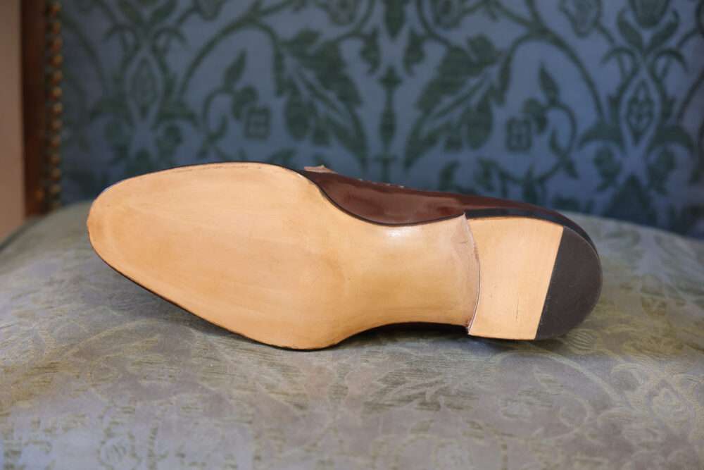 The image shows the sole of a brown leather shoe with a light-colored wooden heel.