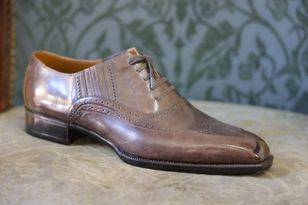 A polished brown leather dress shoe with decorative broguing and a low heel.