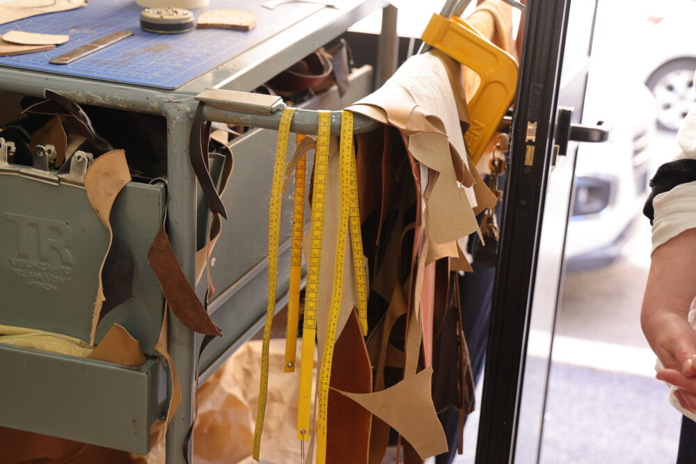 A workbench with various leather scraps and yellow measuring tapes hanging from the side.