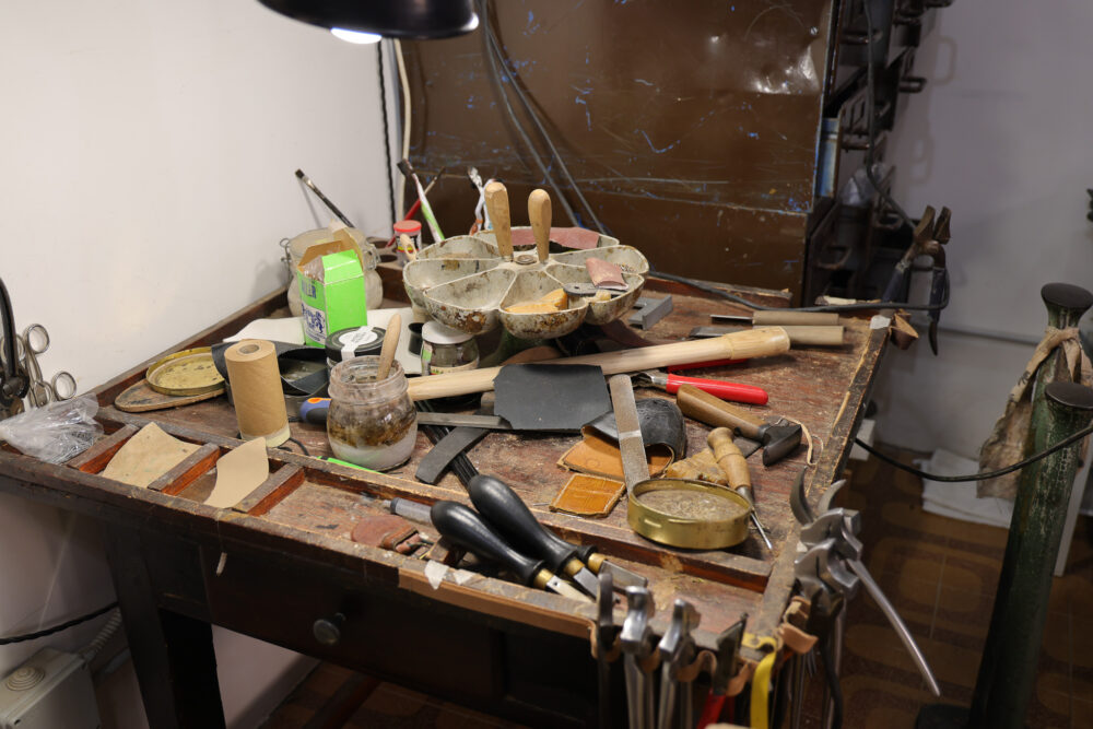 A cluttered shoemaker's workbench with various tools, leather scraps, and containers.