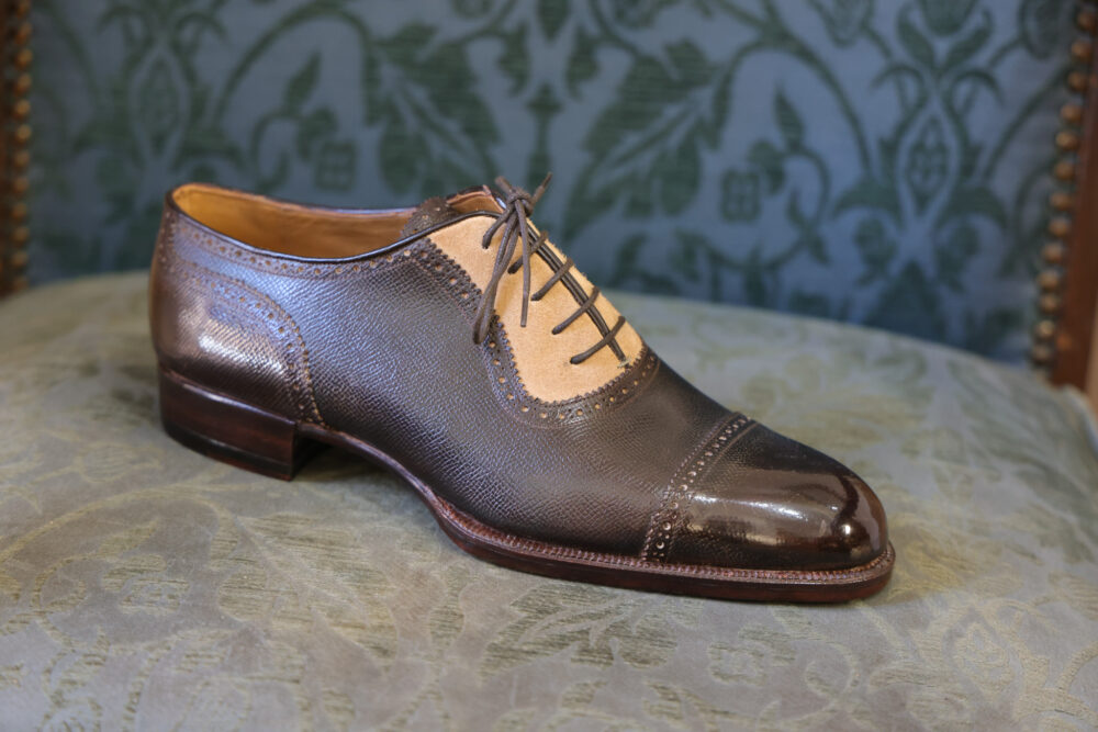A polished brown leather shoe with a suede upper and decorative perforations.