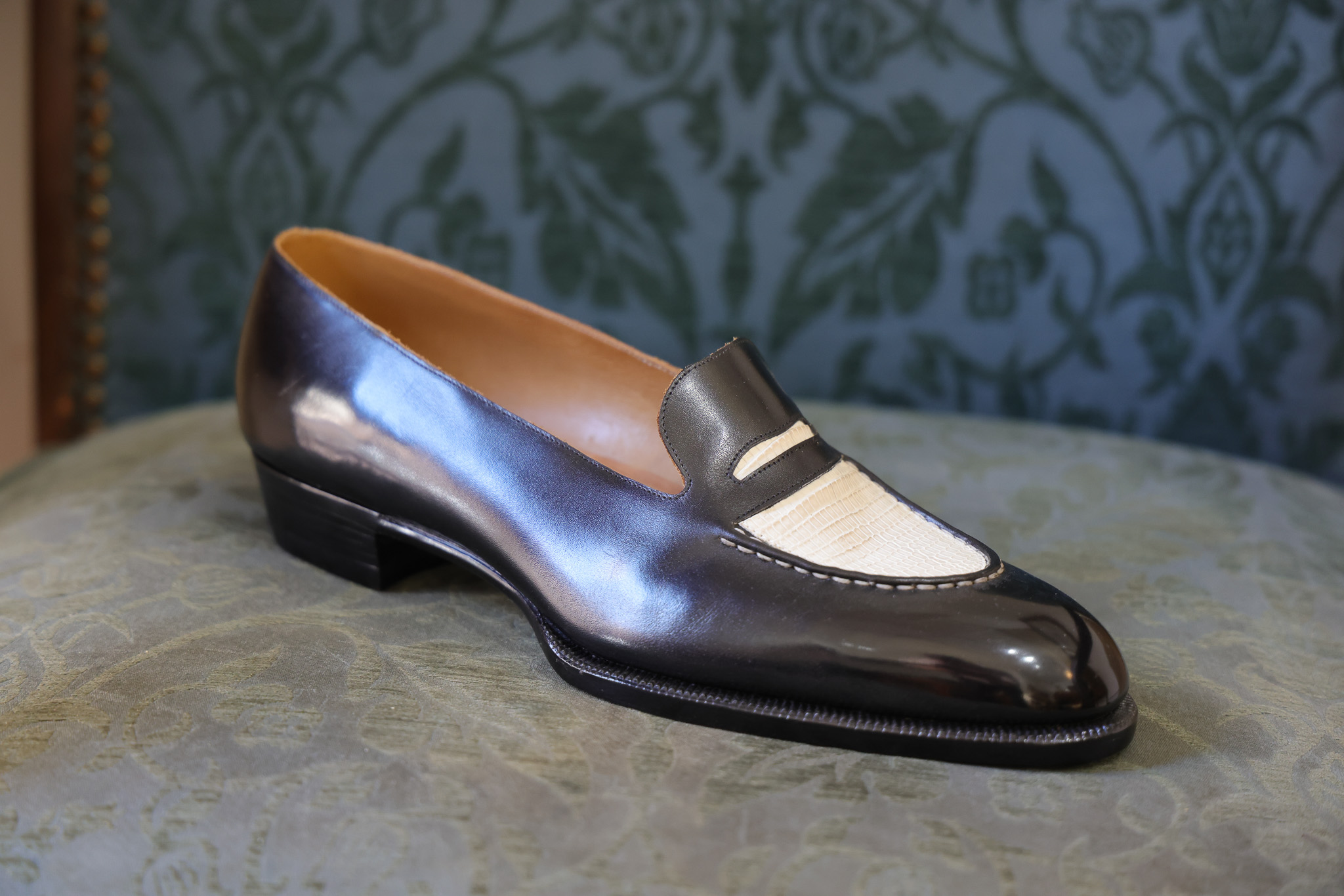 A polished black leather shoe with a cream-colored leather detail on the vamp.