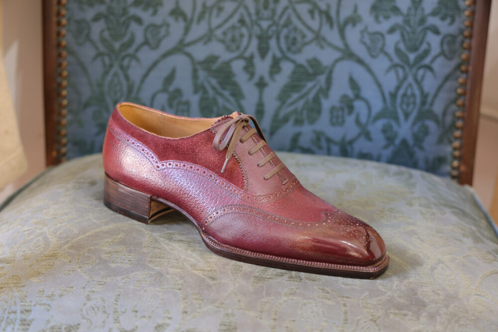 A burgundy leather dress shoe with a brogue design and a low wooden heel.