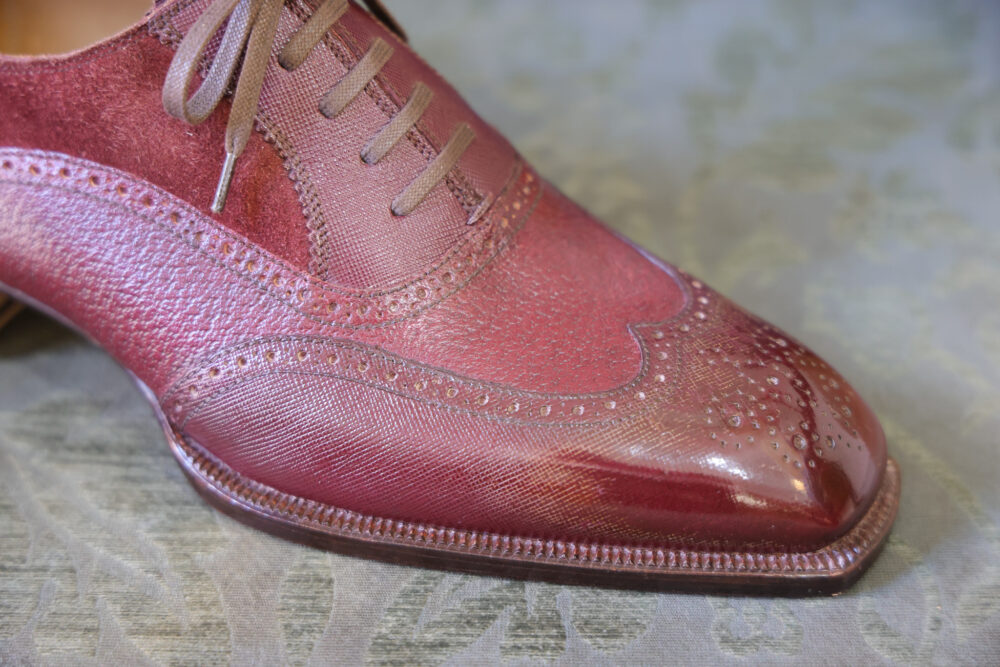 A close-up of a burgundy leather shoe featuring intricate detailing and laces.