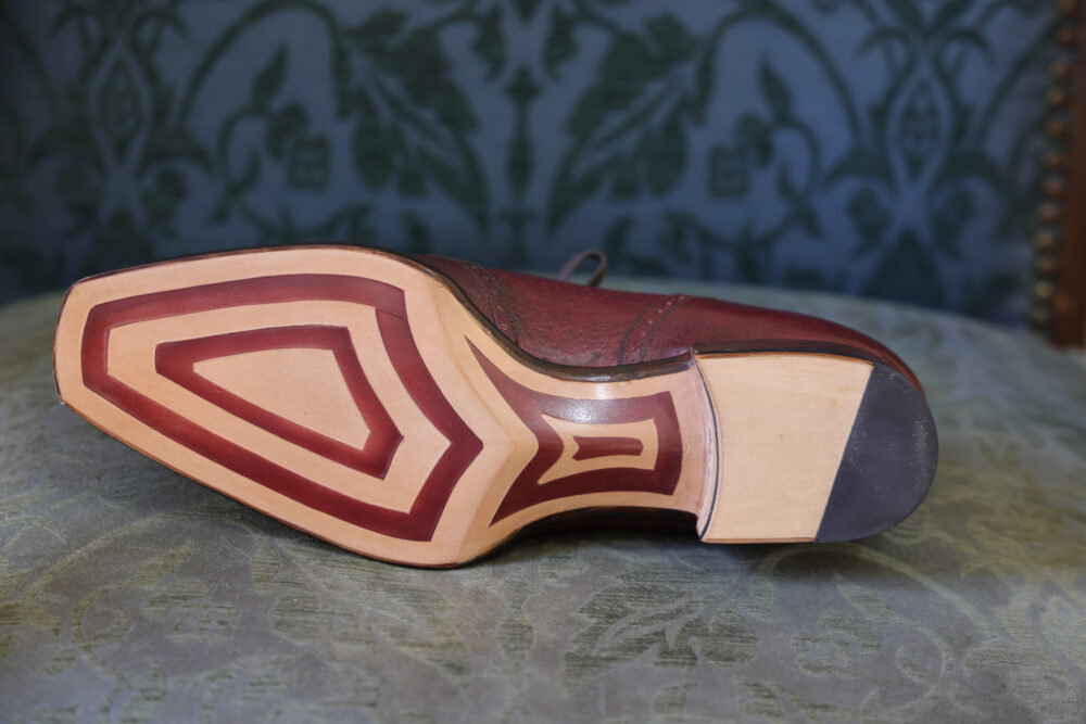 The image shows the sole of a burgundy leather shoe featuring a decorative pattern in a lighter color.