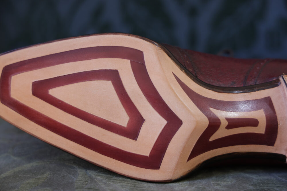 A close-up of a shoe sole featuring a decorative design in light and dark brown leather.