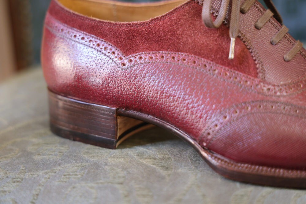 A close-up of a burgundy leather shoe featuring a textured finish and a stacked wooden heel.