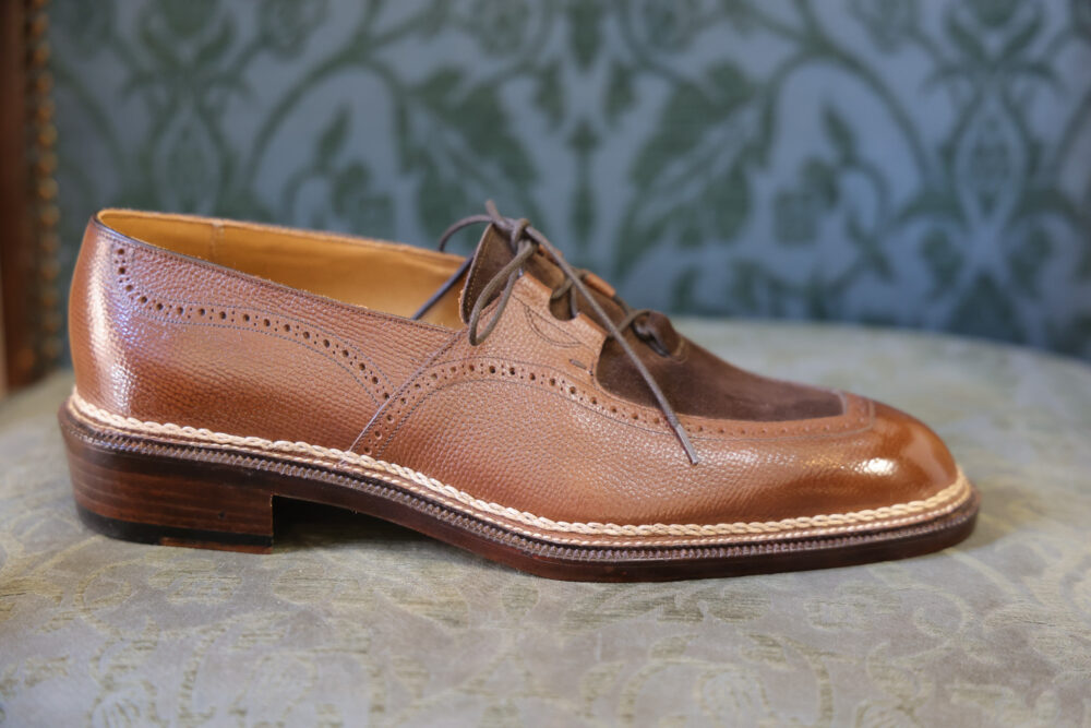 A brown leather shoe with a textured finish and a suede toe cap.