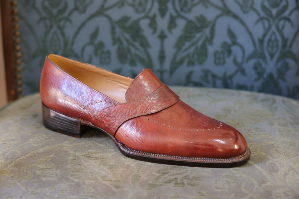 A polished, brown leather shoe with a low heel and decorative stitching.