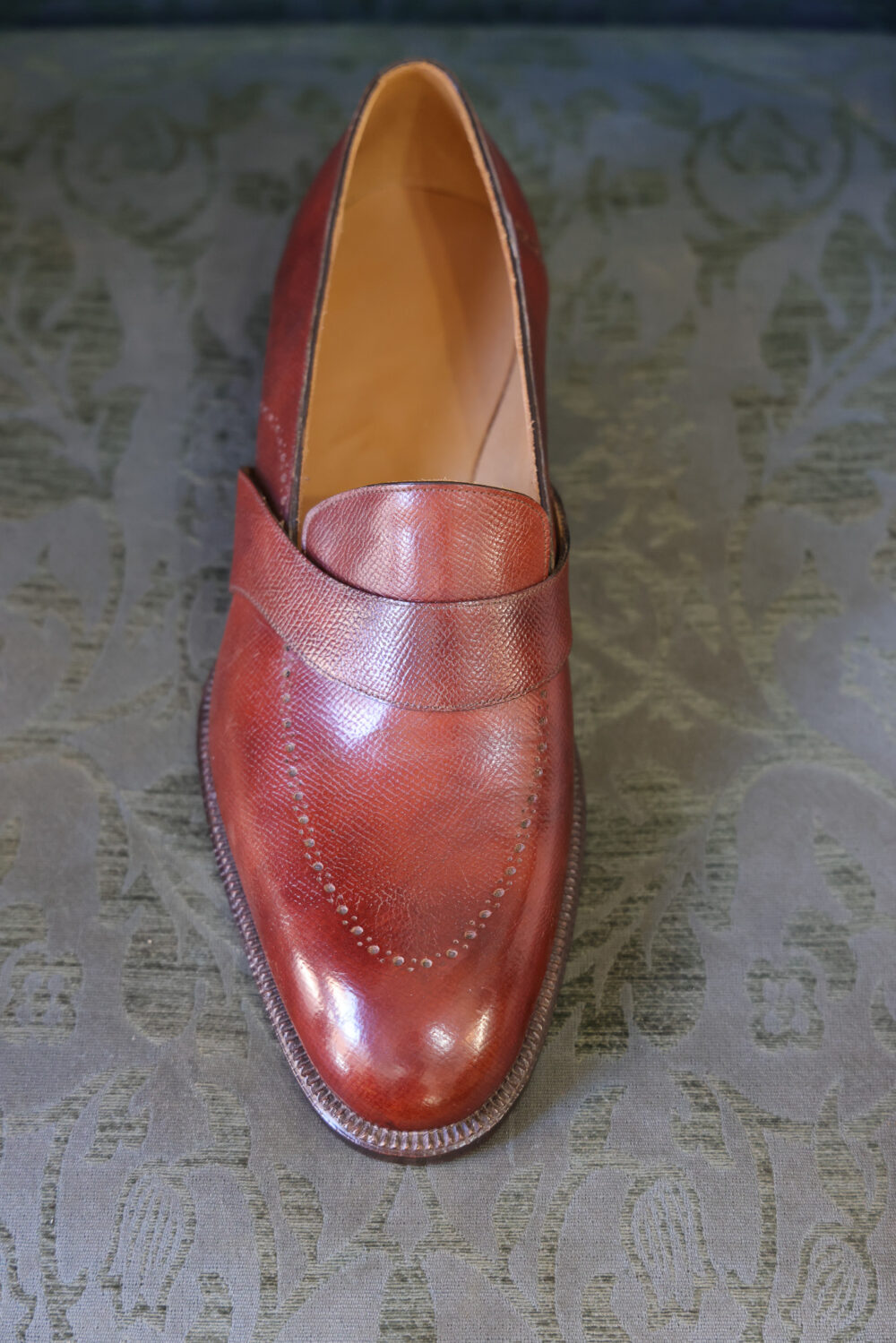 A polished red leather shoe with a decorative strap and stitching details.