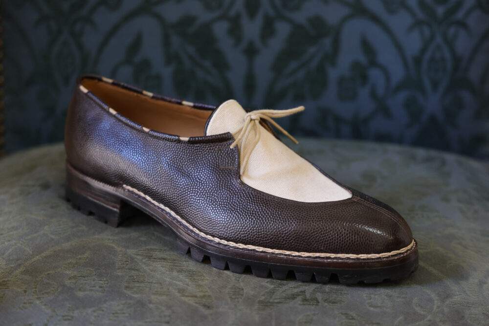 A brown leather shoe with a cream-colored fabric upper and a lace detail.