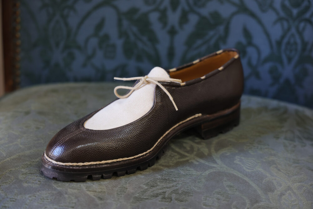 A brown leather shoe with a white fabric toe and a light-colored lace.