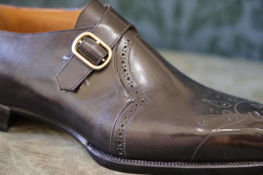 A close-up of a dark brown leather shoe featuring a decorative buckle and intricate detailing.