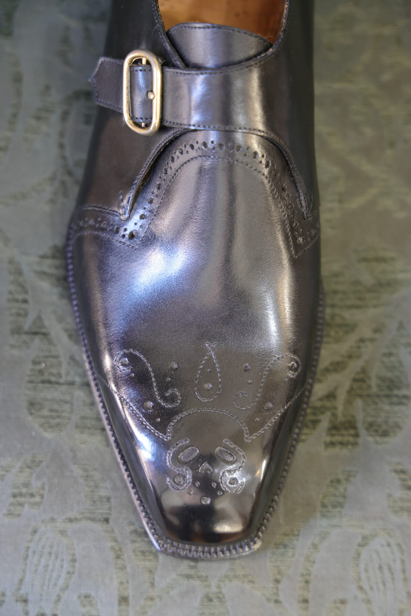 A polished dark leather shoe with intricate detailing and a metal buckle.