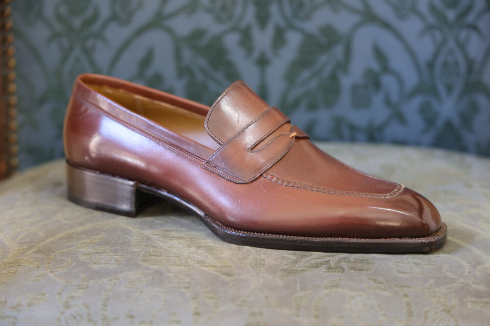 A polished brown leather loafer with a decorative strap and a low heel.