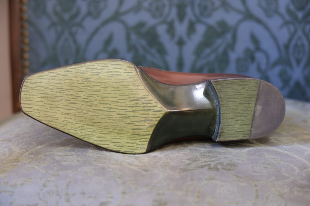 The image shows the sole of a brown leather shoe with a green textured heel.