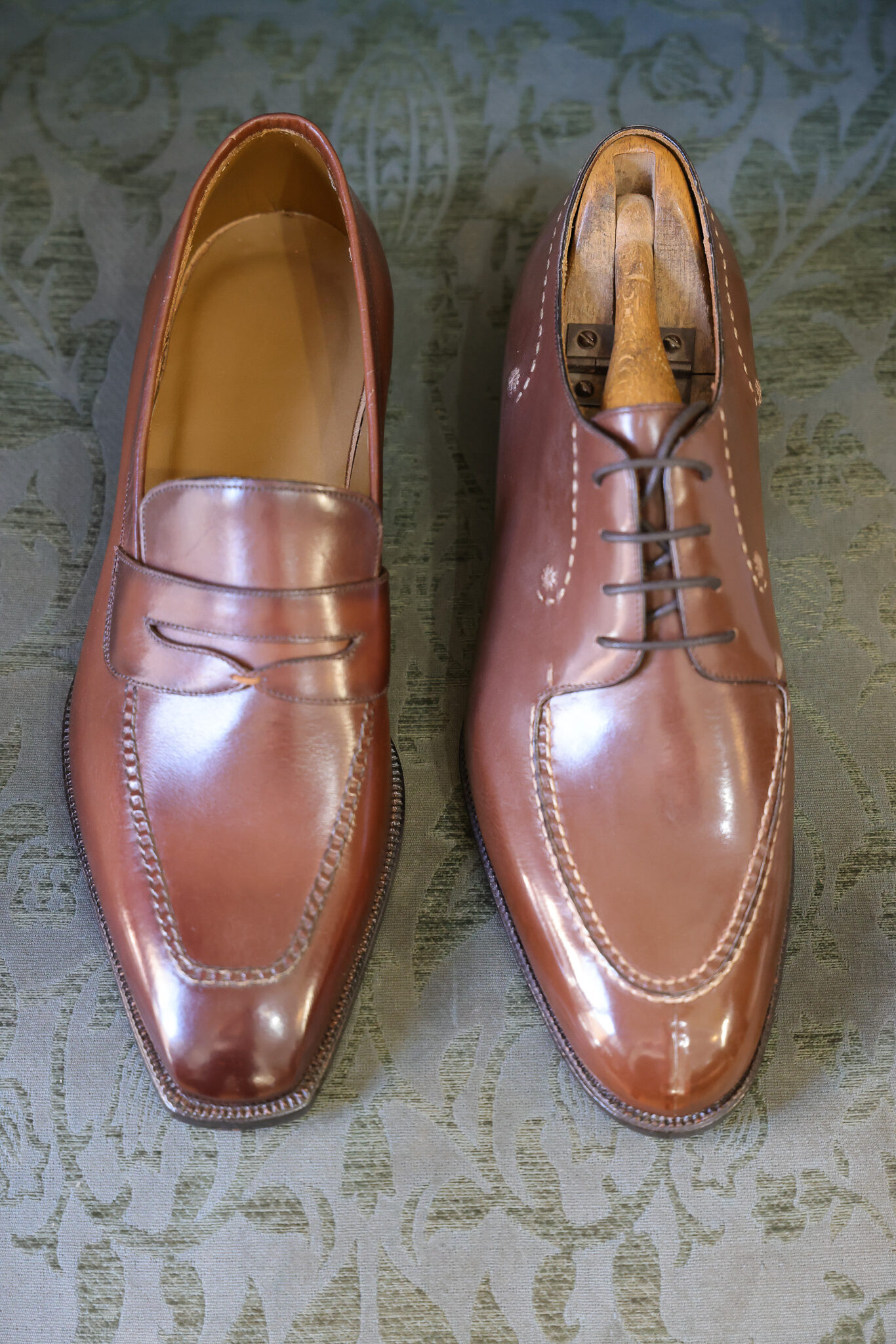 A pair of polished brown leather shoes, one with a loafer design and the other with laces, displayed side by side.