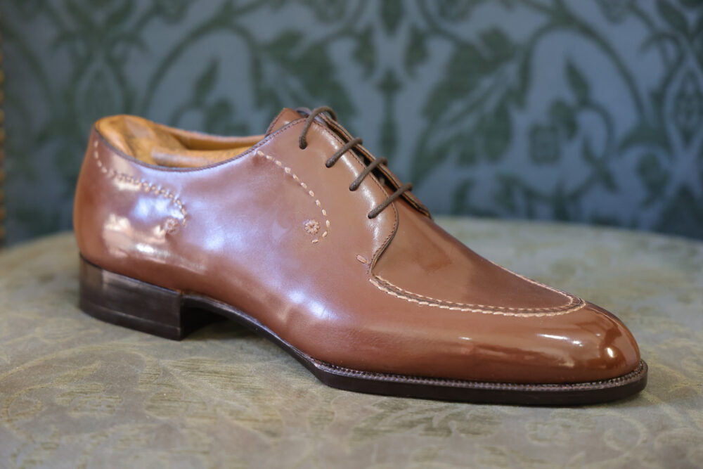 A polished brown leather shoe with decorative stitching and a low heel.