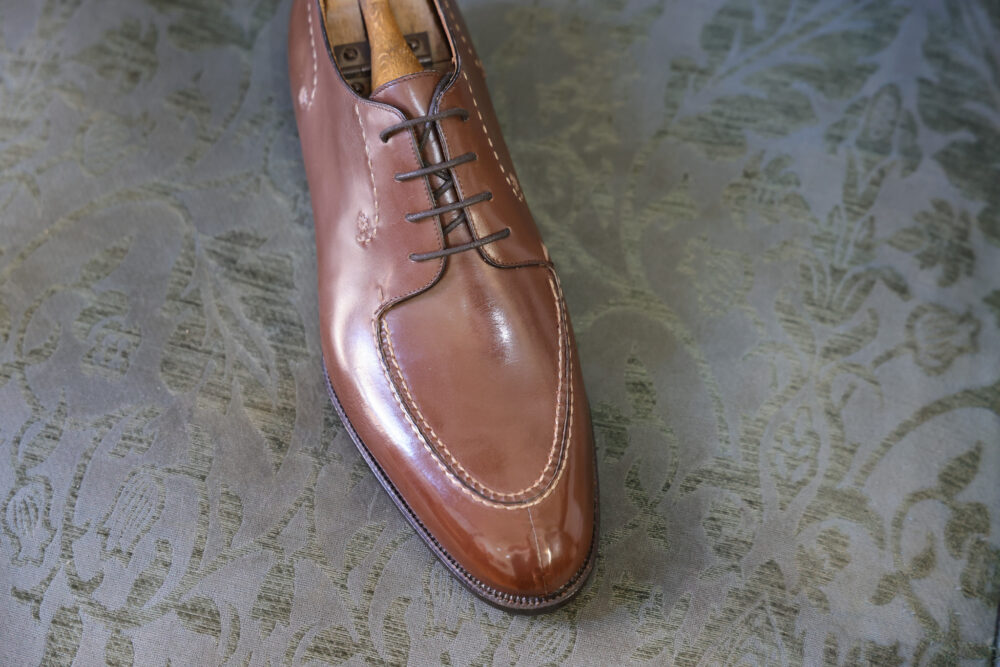 A polished brown leather shoe with laces and a slightly pointed toe.